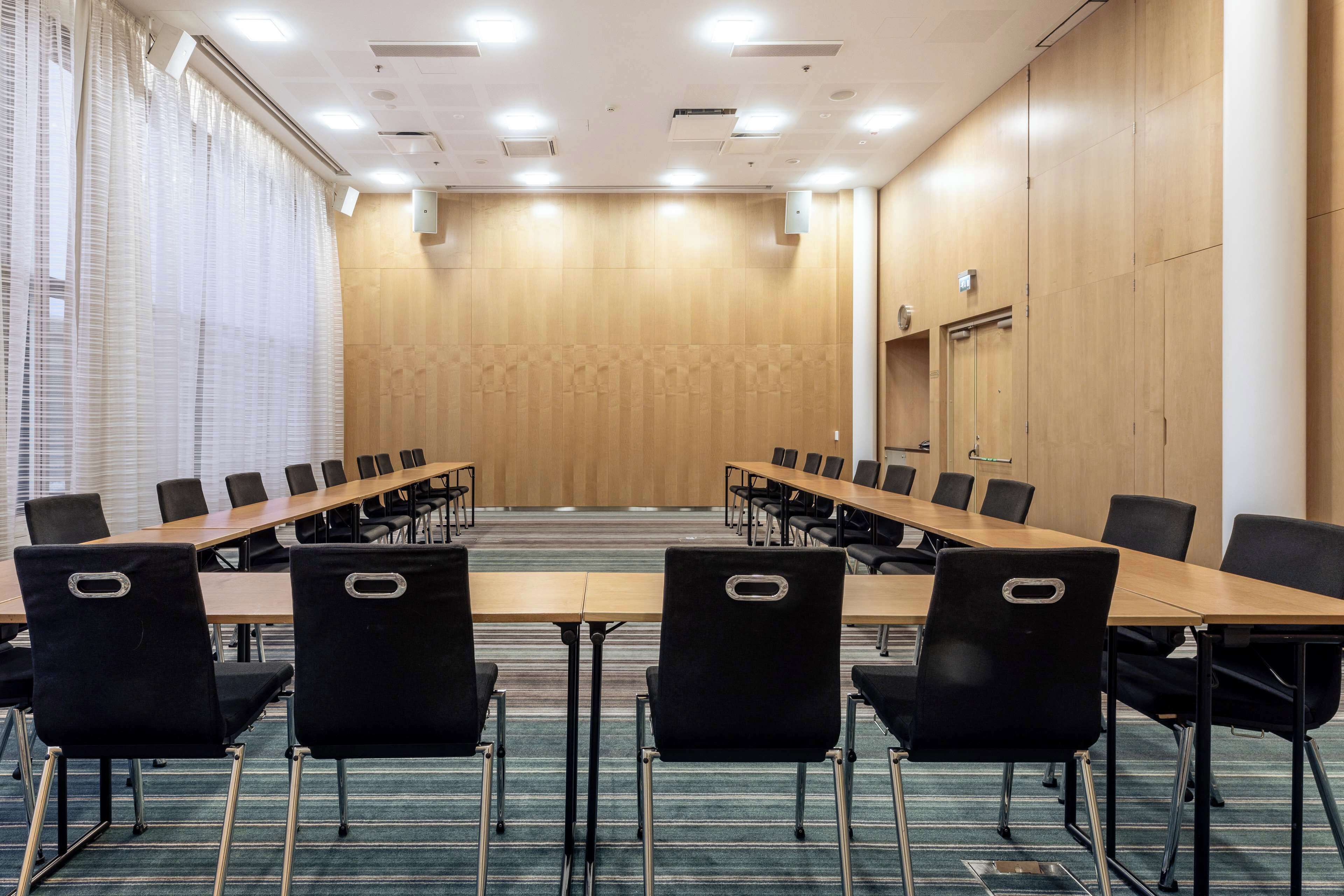 Un salón de conferencias con una mesa larga, sillas negras y paneles de madera.