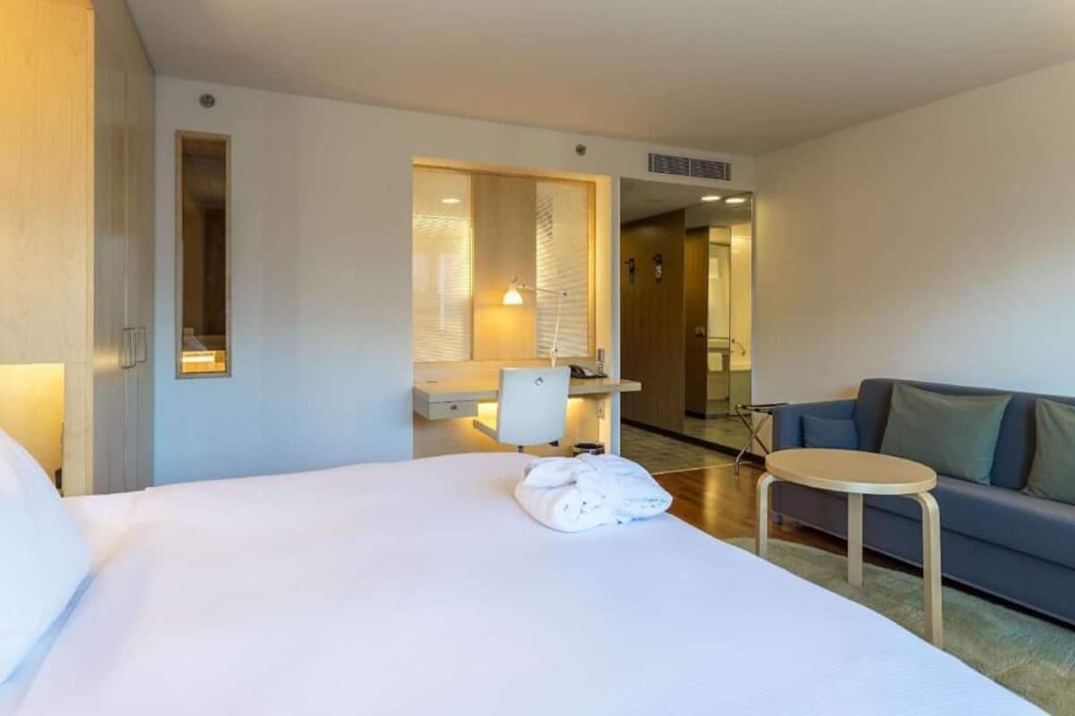 Ein Hotelzimmer mit Bett, kleinem Tisch, einer Couch, Schreibtisch mit Stuhl und Spiegel.