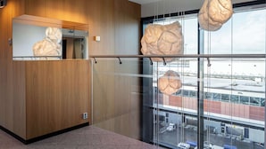 A modern hotel lobby with wooden paneling, a large mirror, and a view of the airport through large windows.