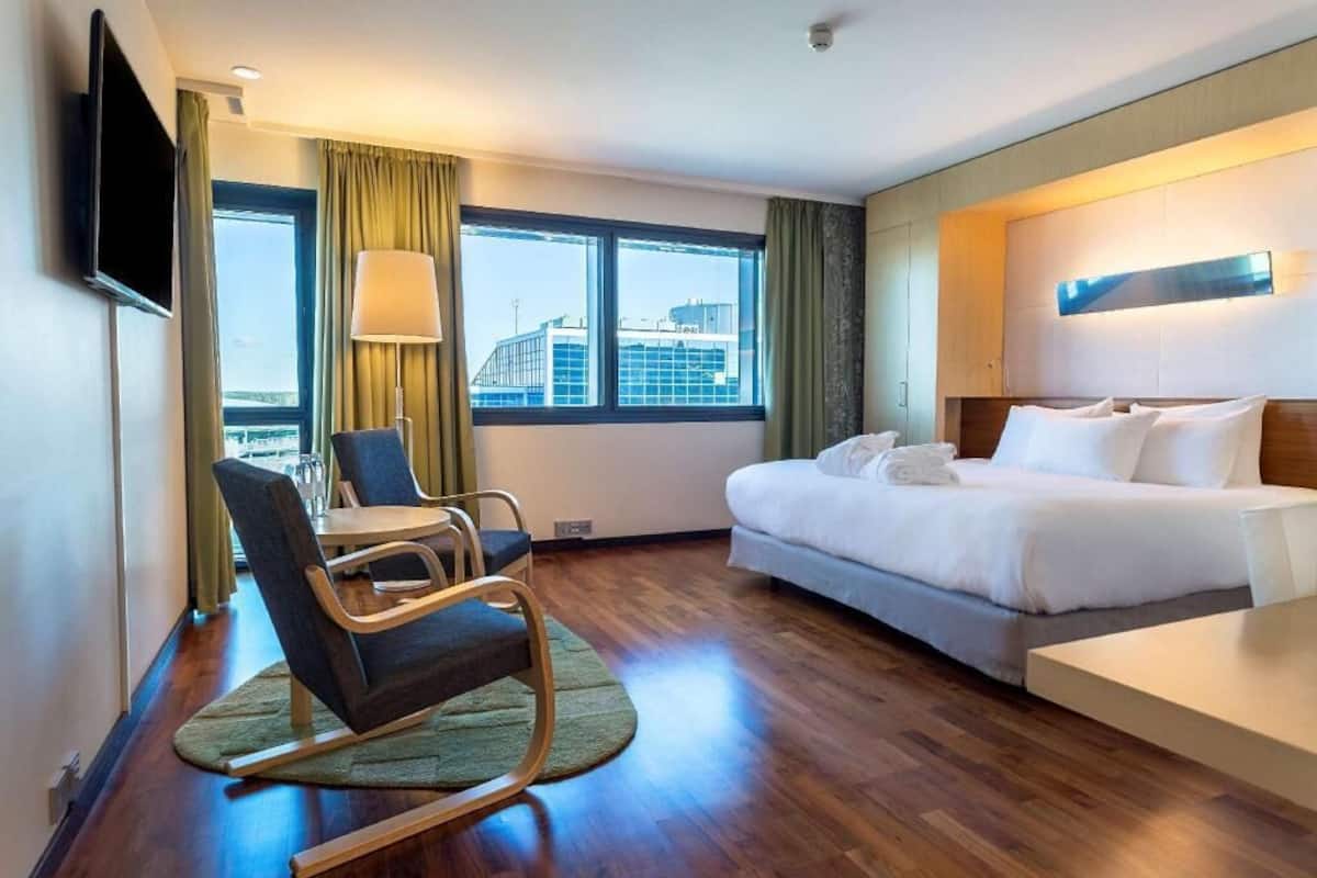 Ein Hotelzimmer mit Bett, Schreibtisch, Stuhl, Fernseher und einem Fenster mit Vorhängen.
