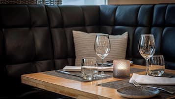 Una mesa de comedor dispuesta con vasos, platos y cubiertos, ubicada frente a un sofá de cuero con un cojín.