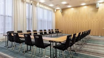 Une salle de conférence avec une longue table et des chaises, de grandes fenêtres équipées de stores et un mur en bois.