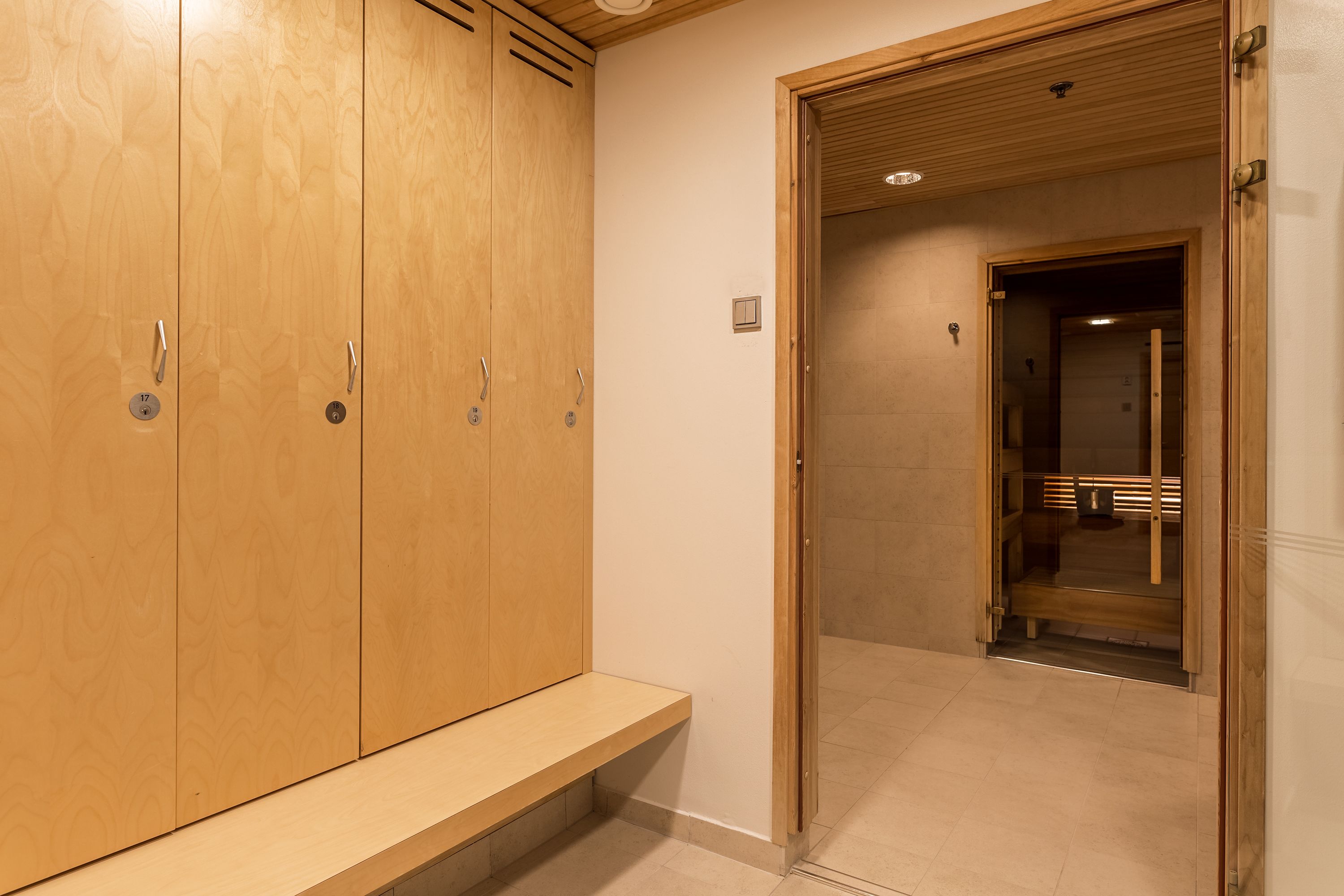 Vestuario de madera con bancos y una puerta que da a una zona de duchas.