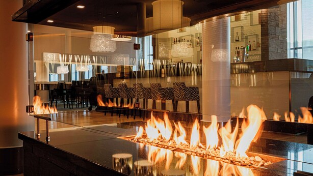 A bar area with a central fire feature, seating, and a modern interior design.
