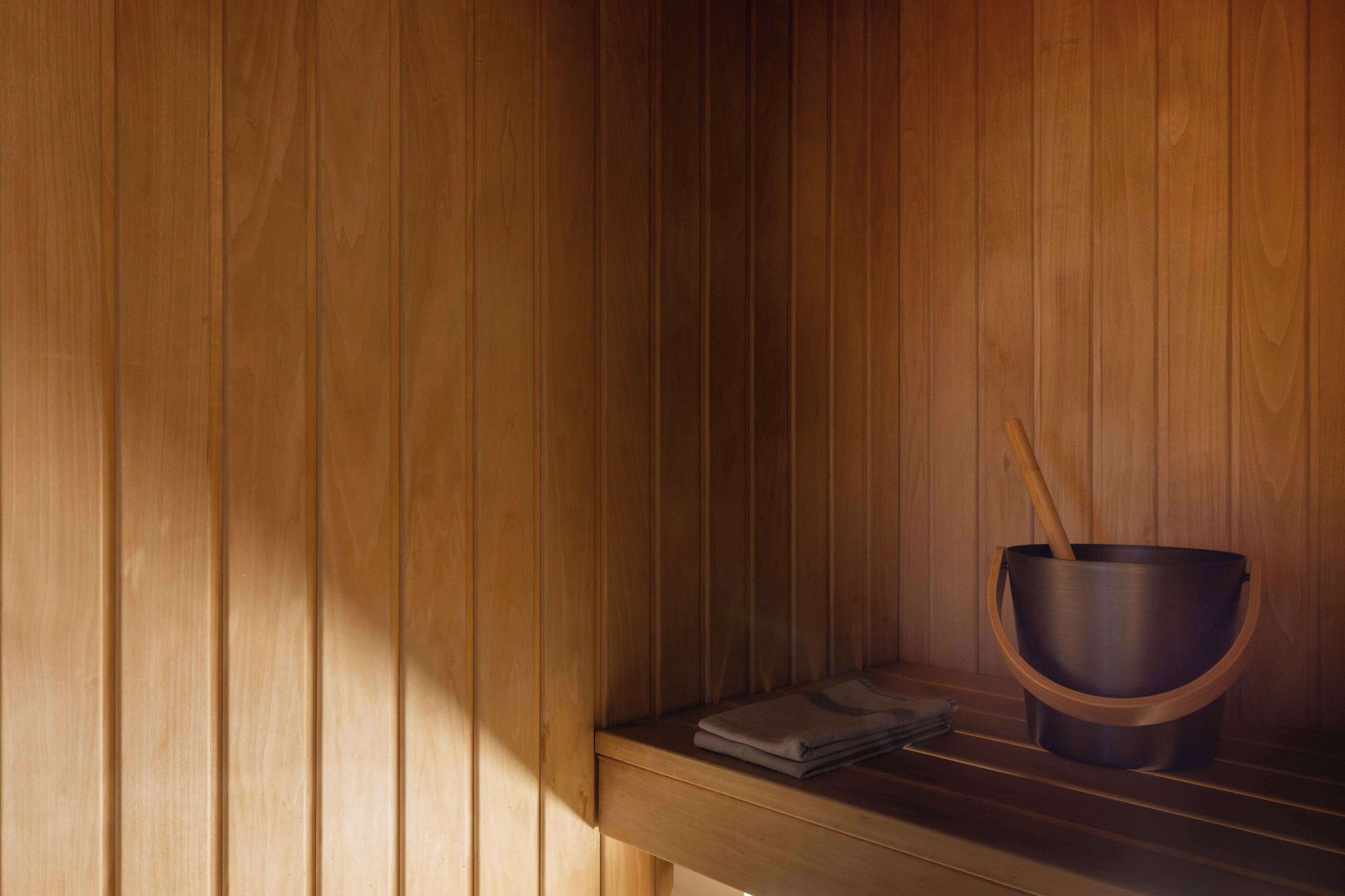 A sauna with wooden walls, a bench, a bucket, and a folded towel.