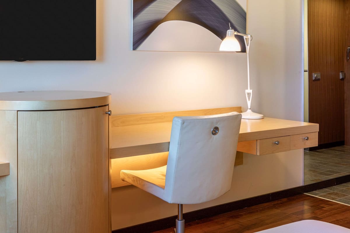 Ein Hotelzimmer mit Schreibtisch aus Holz, einem Sessel, einem Flachbildfernseher und einem Bild an der Wand.