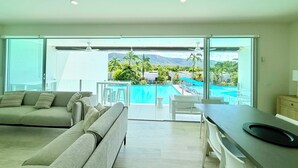 A modern living room with a sofa, a dining area, and a view of a swimming pool and mountains.
