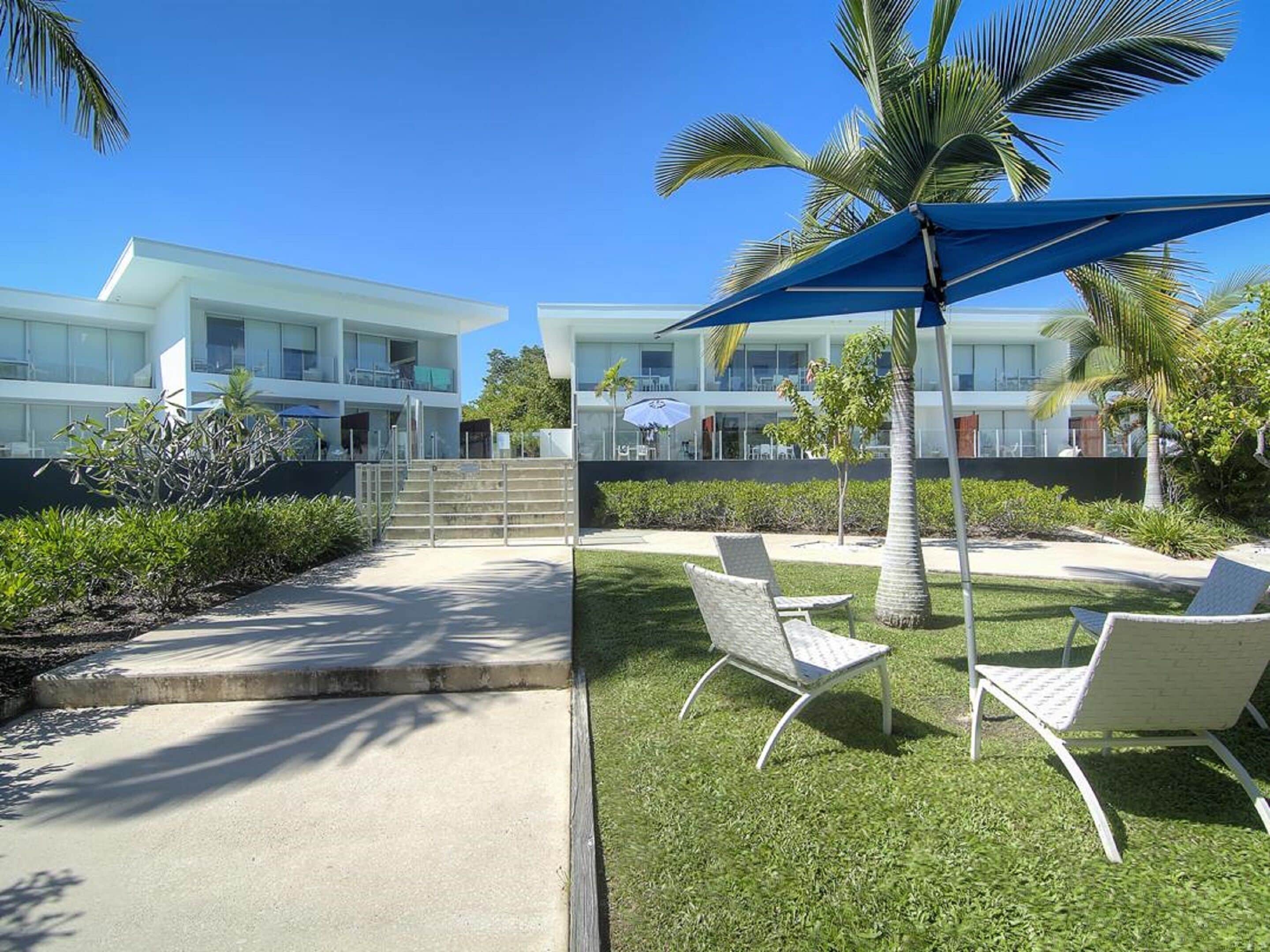 A modern building with a pool area, outdoor seating, and palm trees.