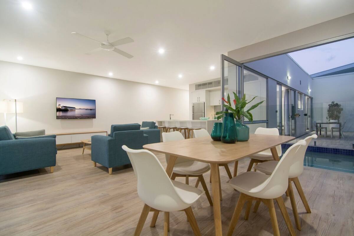 A modern living room with a wooden dining table, white chairs, and blue sofas.