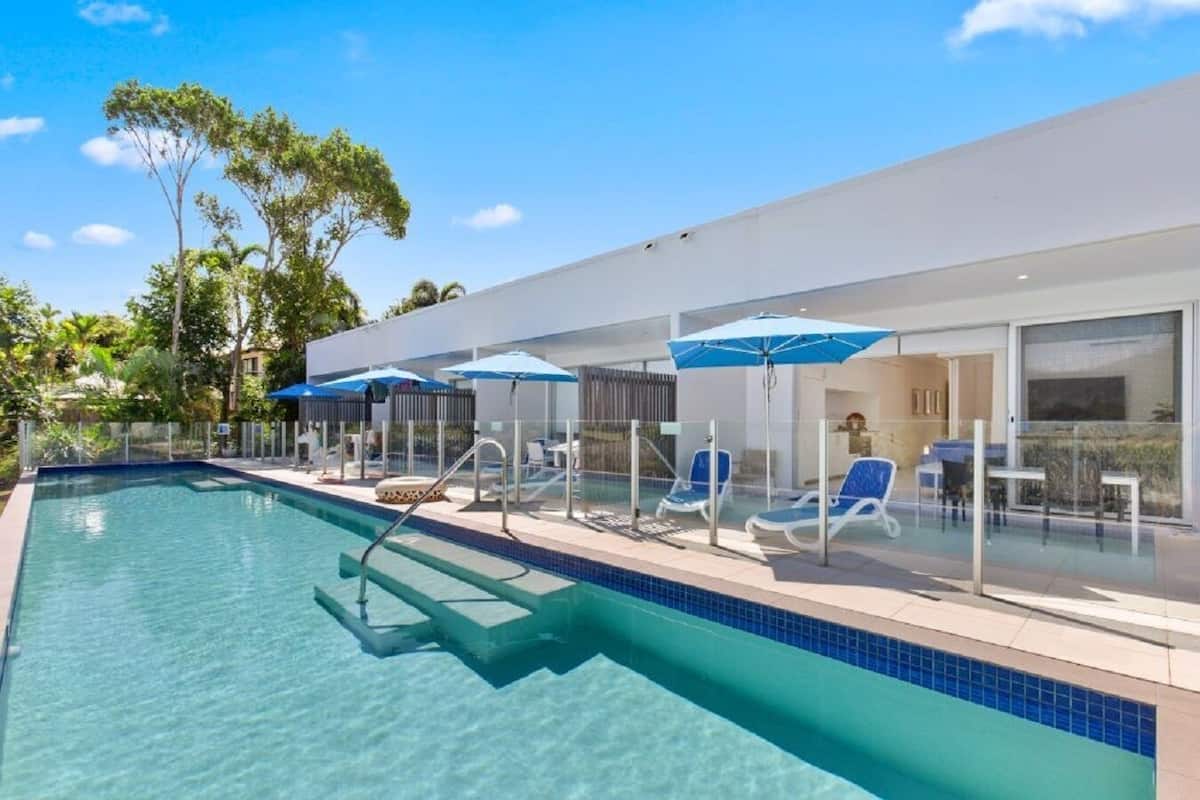 A modern pool area with clear blue water, sun loungers, and umbrellas.