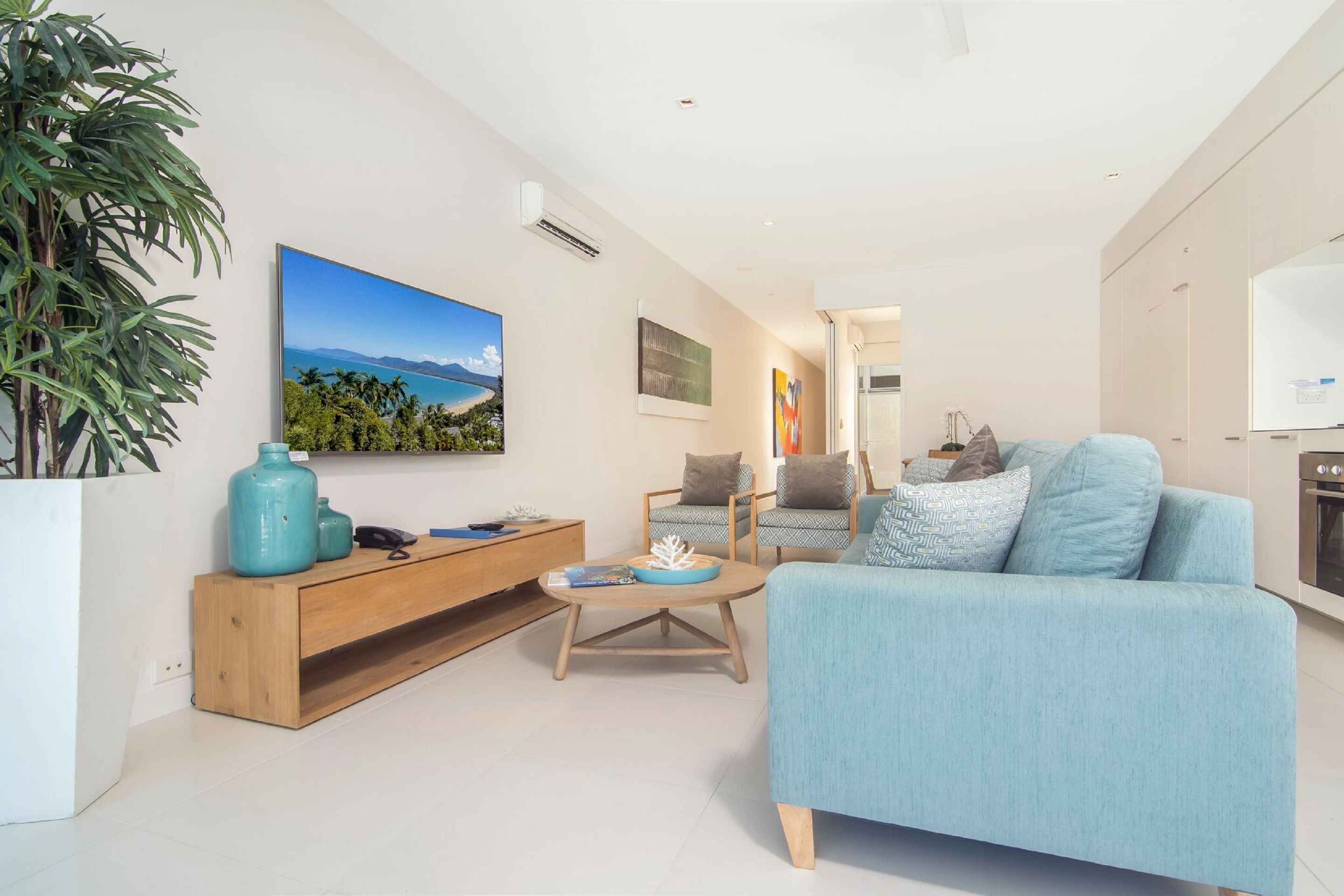 Una sala de estar moderna con un sofá azul, una mesa de centro de madera y un televisor grande en la pared.