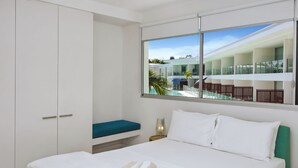 A hotel room with a bed, a window with a view of the pool and outdoor seating, and a white wardrobe.