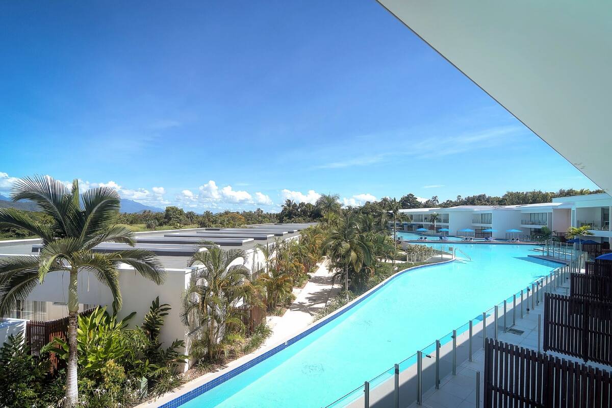 A swimming pool with a curved edge, surrounded by palm trees and a white fence.
