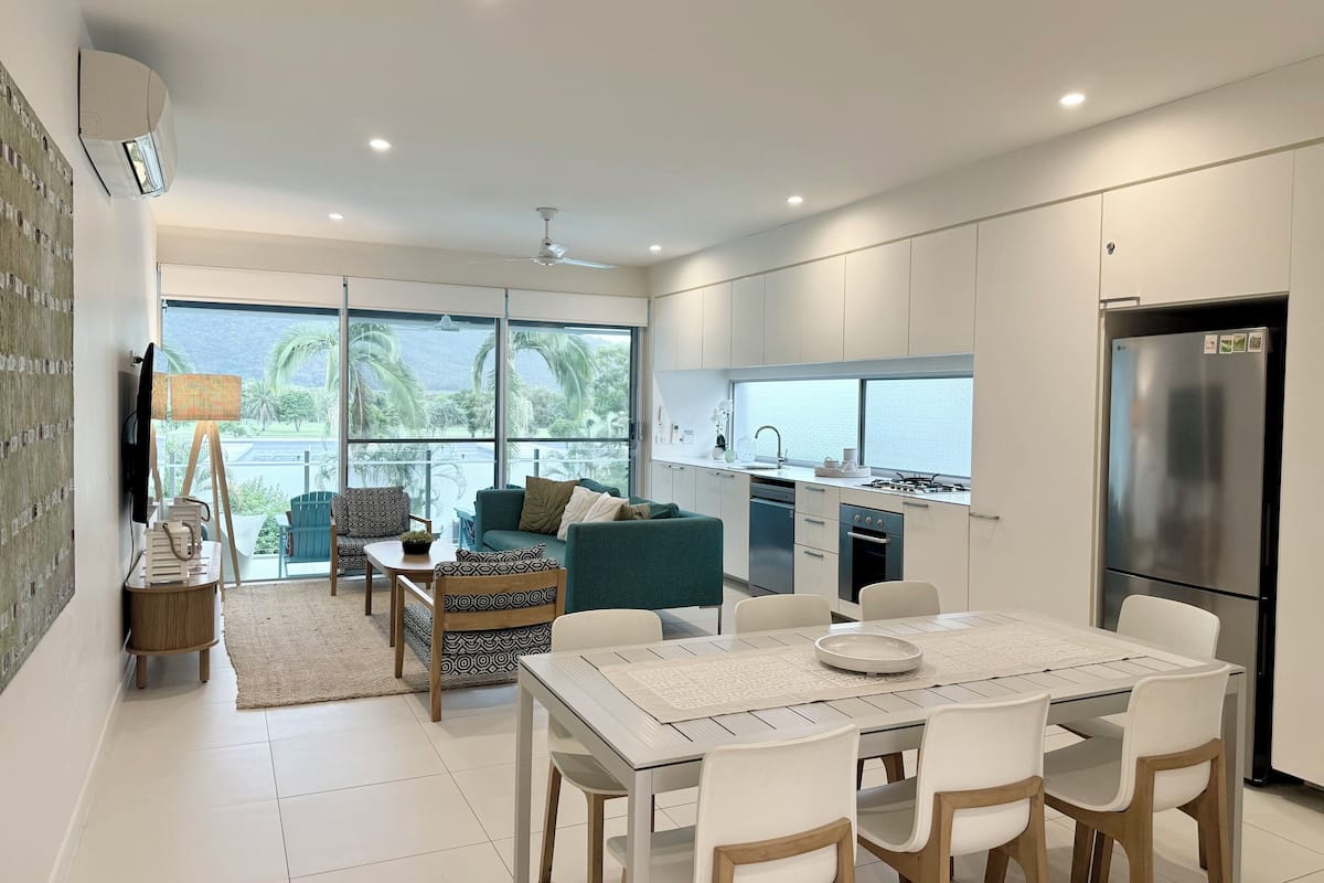 A modern kitchen with a dining area, large windows, and a view of the outdoors.