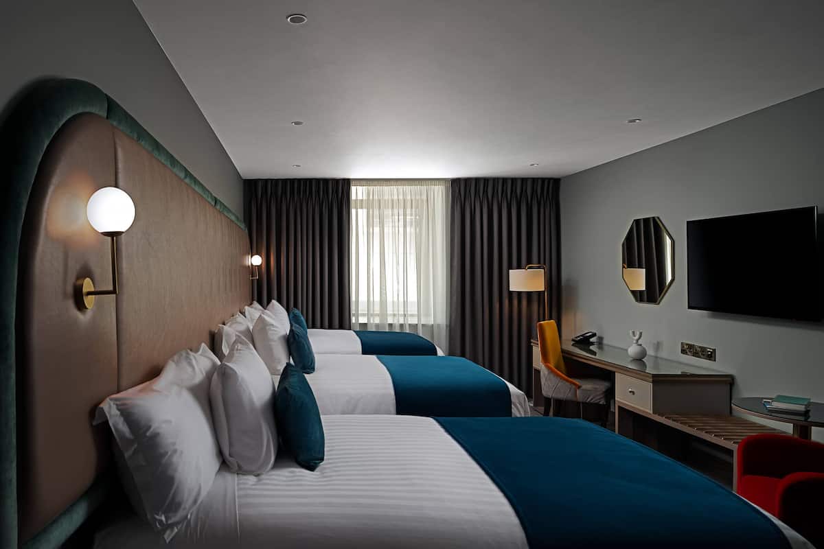 A hotel room with two beds, a desk, a chair, a TV, and a window with curtains.