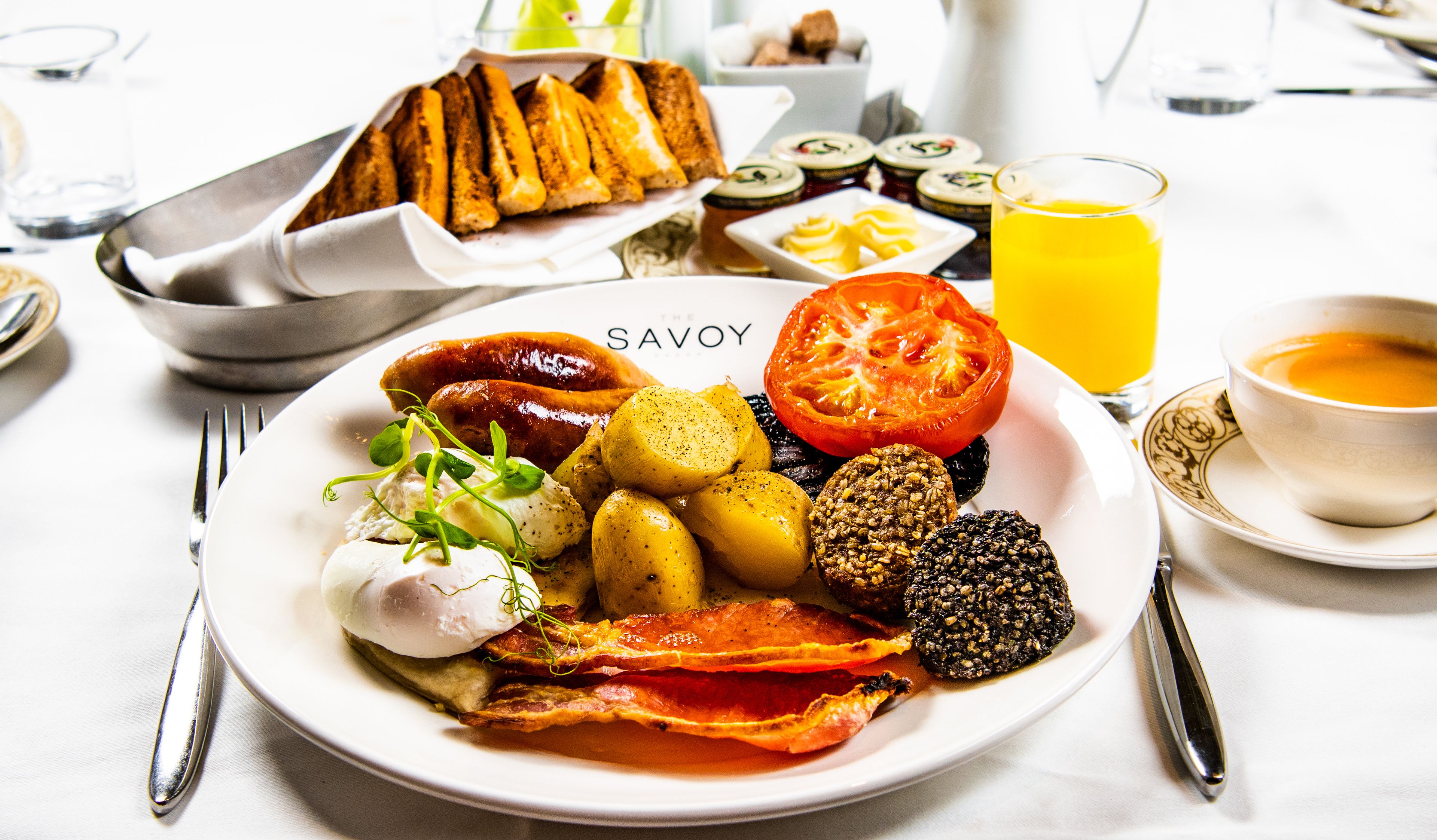 A breakfast plate with eggs, bacon, sausages, and vegetables.
