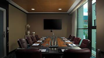 A conference room with a long table, red chairs, a flat-screen TV, and a large window.