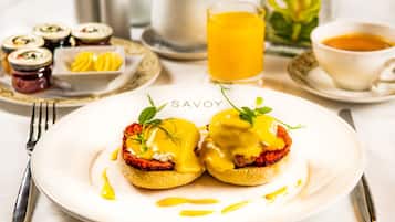 A breakfast setting with eggs benedict, a glass of orange juice, and various side dishes.