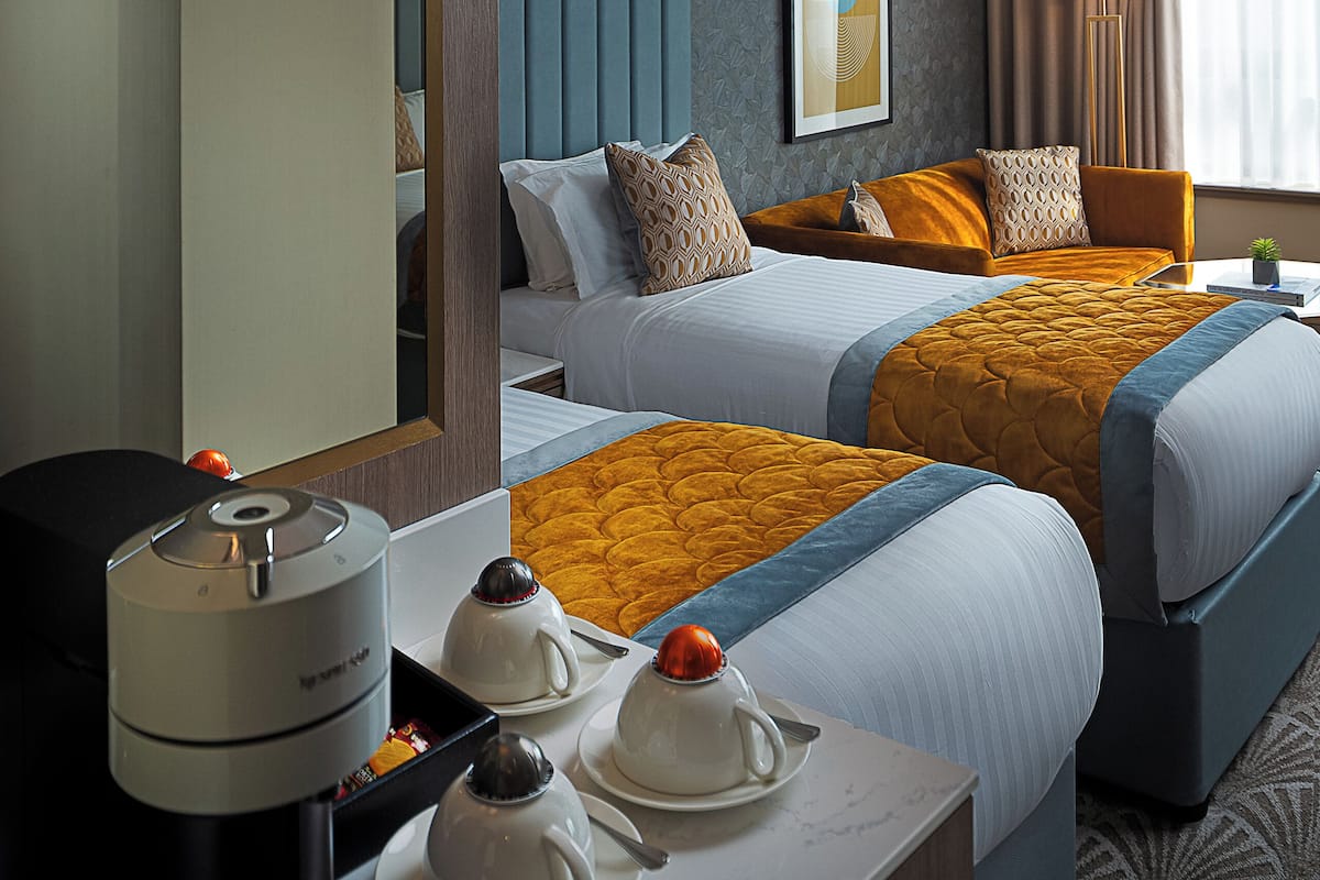 A hotel room with two beds, a coffee maker, and a table with teapots.
