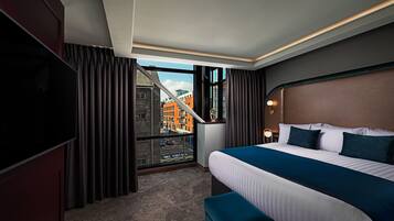 A hotel room with a large bed, a TV, a view of the city through a window, and a balcony.