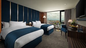 Une chambre d’hôtel avec deux lits, un bureau, une chaise, une télévision et une vue sur la ville.