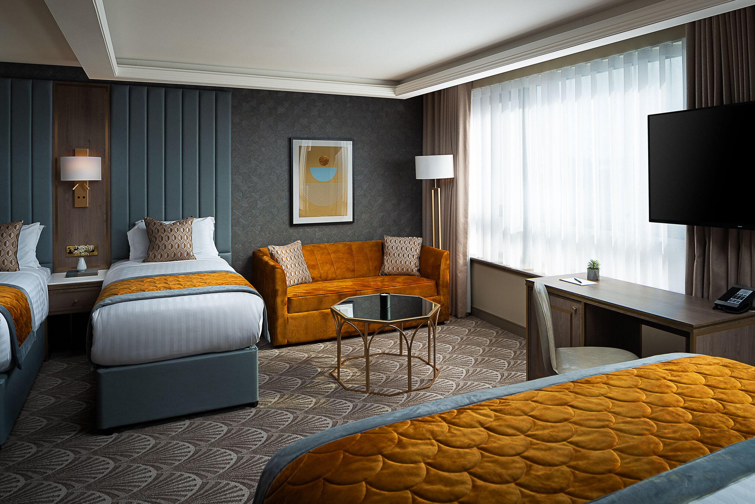 A hotel room with two beds, a sofa, a desk, and a TV.