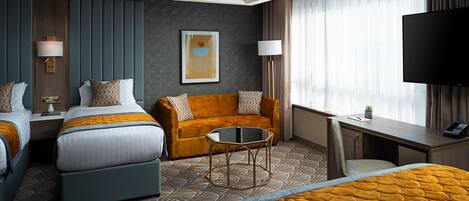 A hotel room with two beds, a sofa, a desk, and a TV.