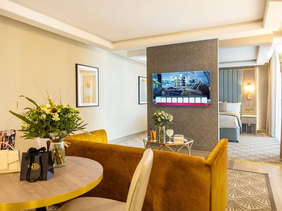 Habitación de hotel con sofá, una mesa con un florero, televisor en la pared y cama con cabecera.