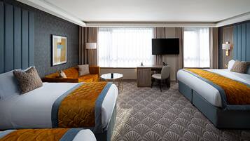 A hotel room with two beds, a desk, a chair, a TV, and a large window with curtains.