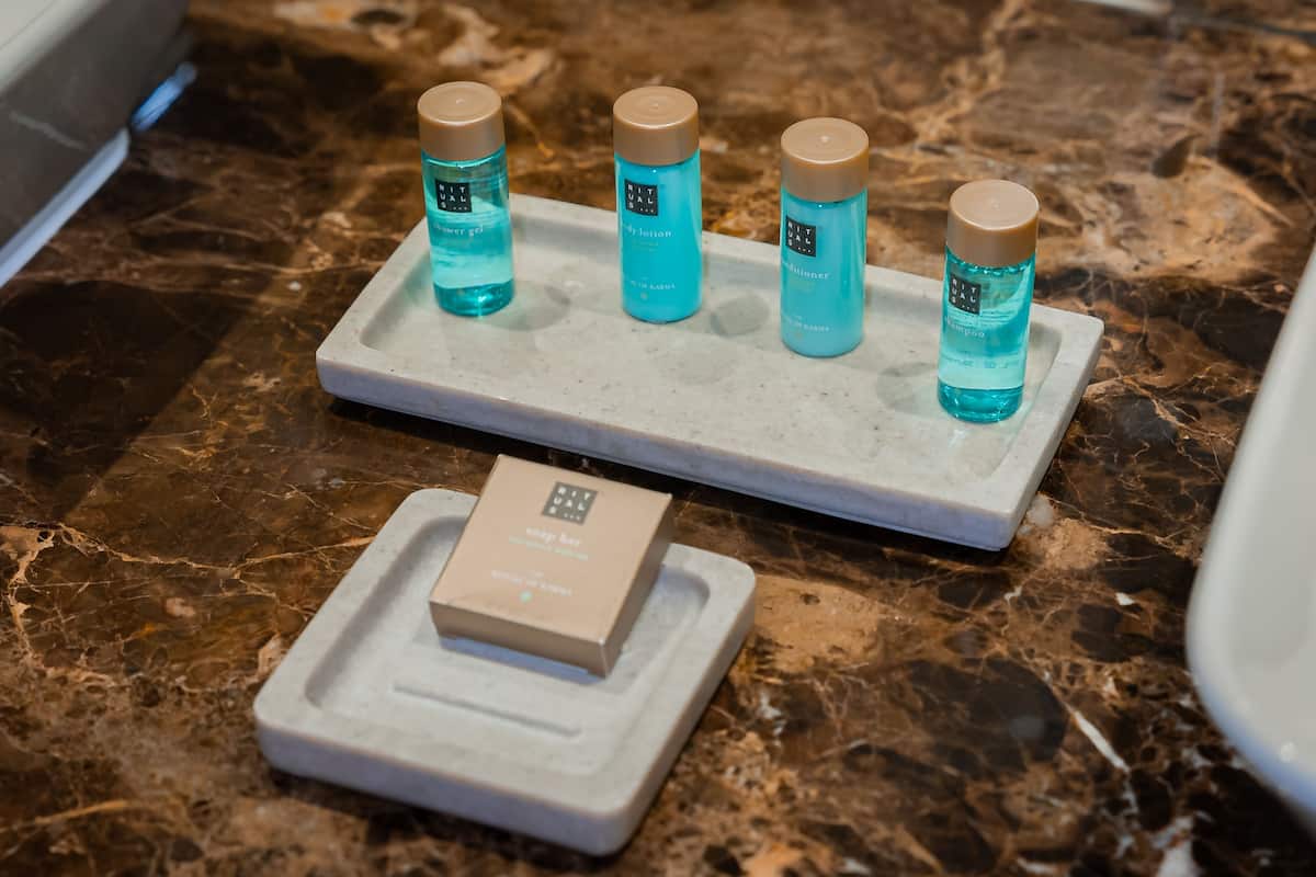 Un lavamanos de baño con encimera de mármol, mostrando tres botellas de productos capilares y una pastilla de jabón.