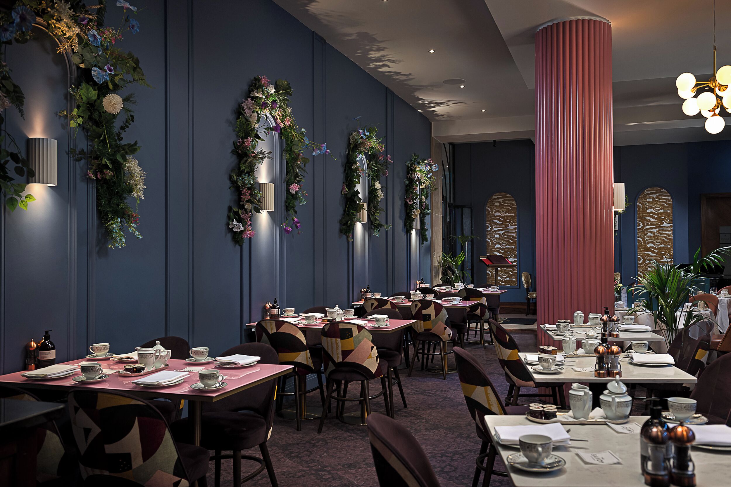 Comedor con mesas dispuestas para el servicio, paneles decorativos en la pared y una columna alta.