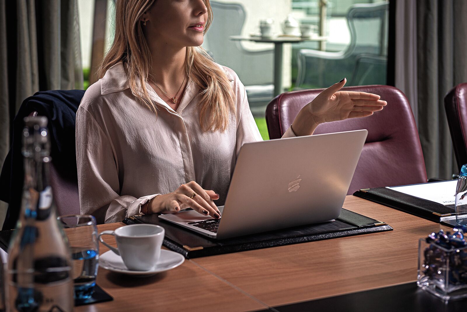 A person working on a laptop in a modern office setting with leather chairs and a glass table.