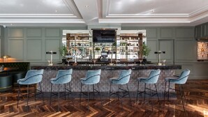 Un espace bar doté d’un parquet en bois disposé en chevrons, d’un comptoir central et de cinq tabourets de bar.