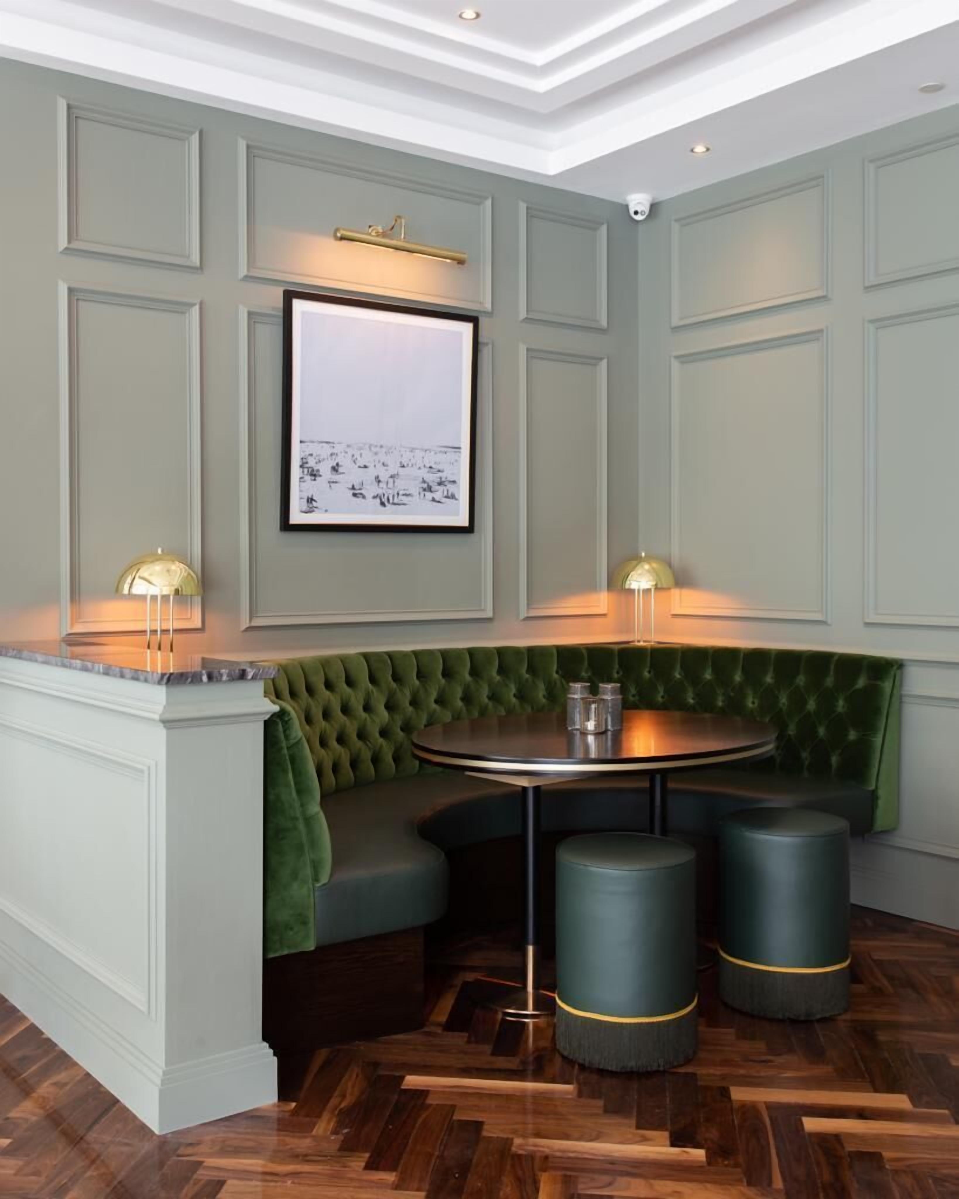 A corner seating area with a round table, green upholstered bench, and two stools.