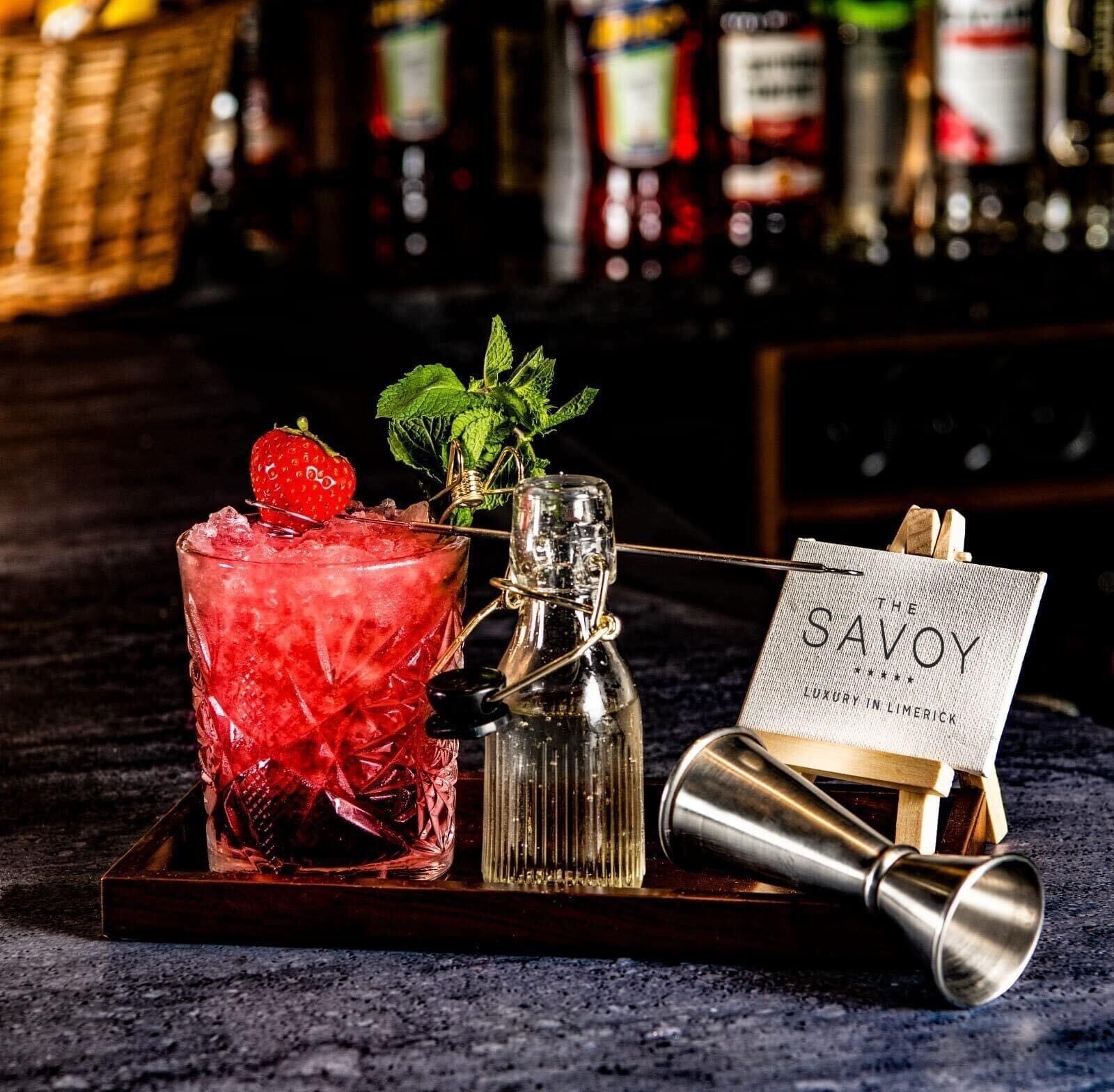 A bar setting with a cocktail glass, a bottle, and a metal shaker on a tray.