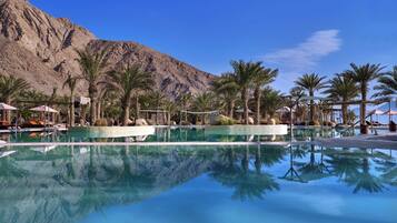 A pool with clear blue water, surrounded by palm trees and a mountain in the background.