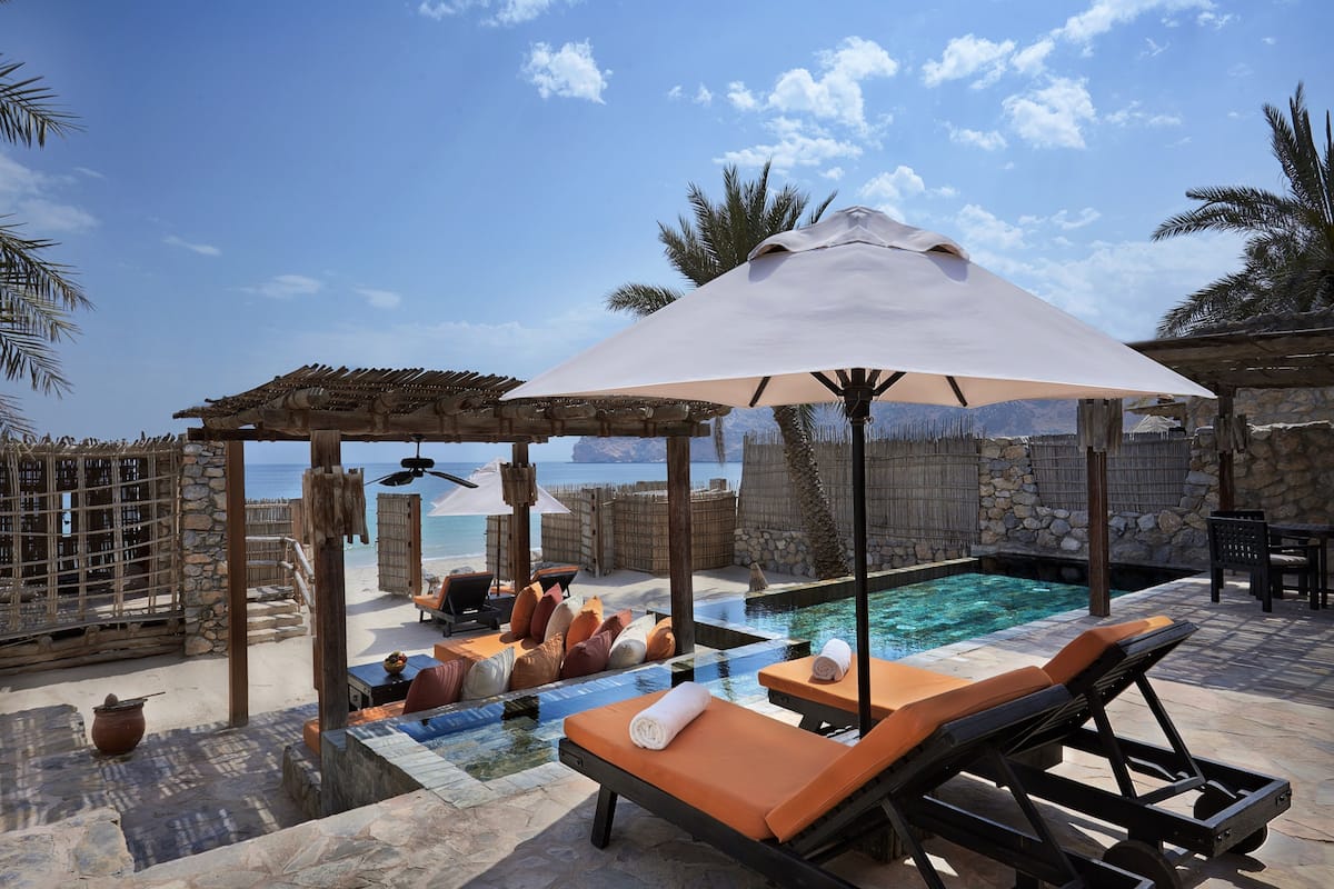 Ein Poolbereich mit Liegestühlen, einer Pergola und Blick auf das Meer.