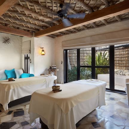 A spa room with two massage tables, a ceiling fan, and a view of the outdoors.