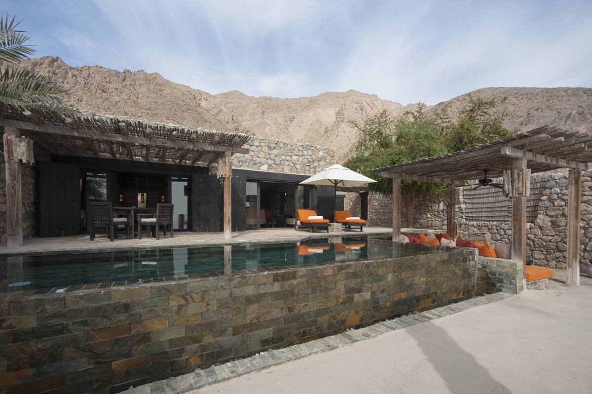 Ein Poolbereich mit Steinmauern, Liegestühlen und einer Pergola.
