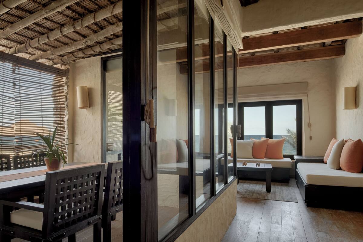 Ein modernes Interieur mit Essbereich, Sitzgelegenheiten mit Kissen und großen Fenstern mit Blick.