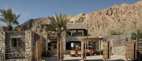 A stone building with a modern design, featuring a patio area with outdoor seating and palm trees.