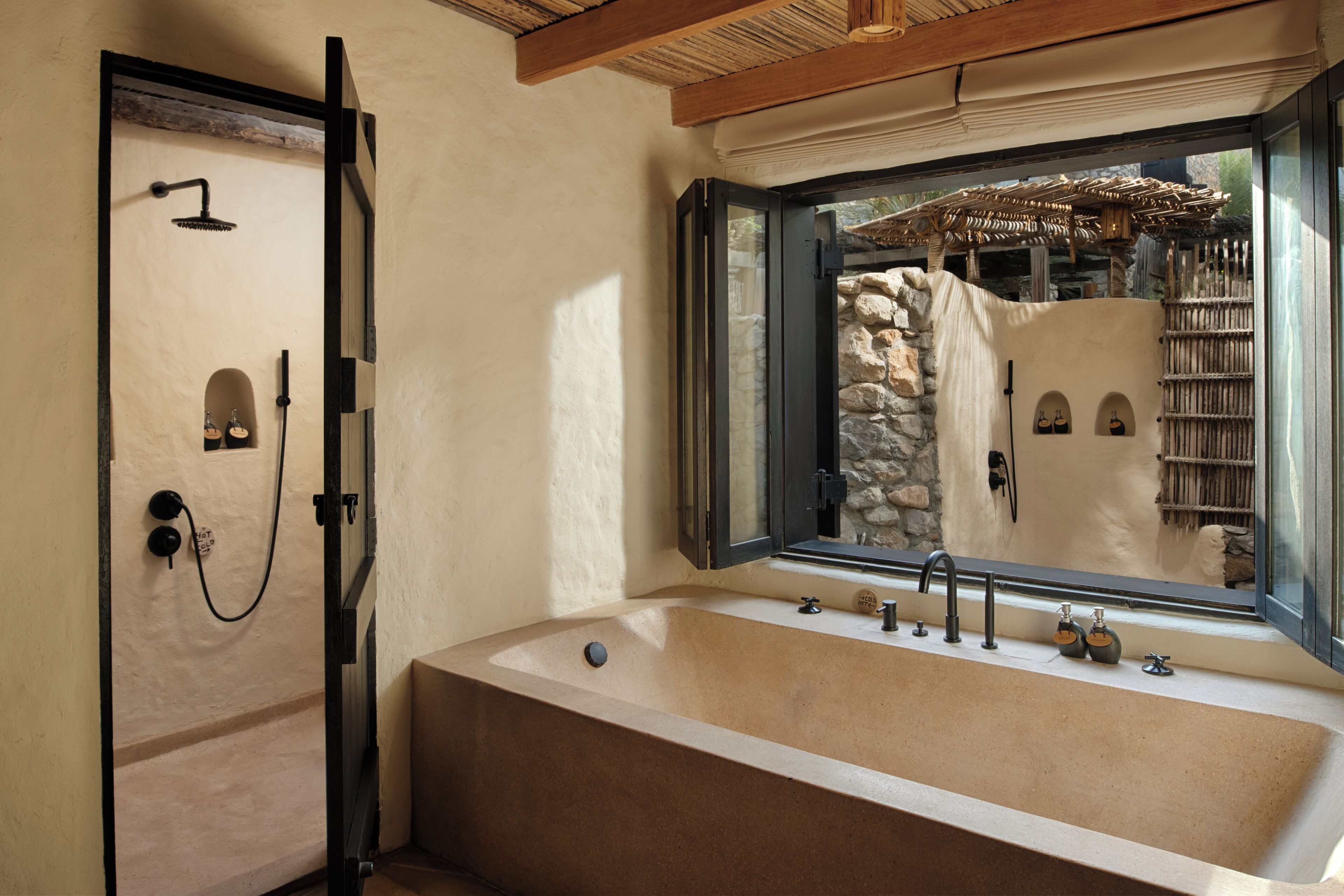 Un baño con una bañera grande, ducha y ventana con vistas a un muro de piedra y una estructura de madera.
