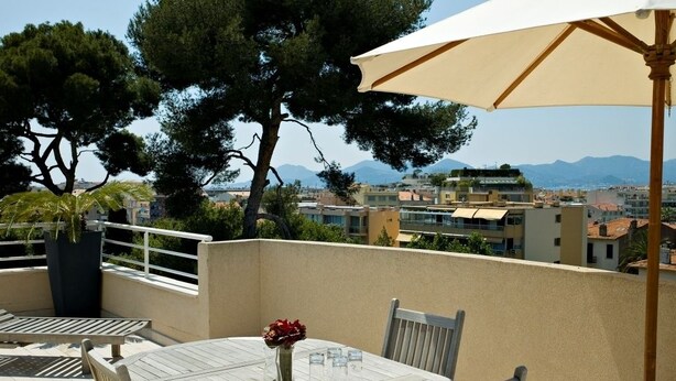 A terrace with a table set for dining, surrounded by trees and a view of the city and mountains. - PAVILLON BEL AIR (Cannes)