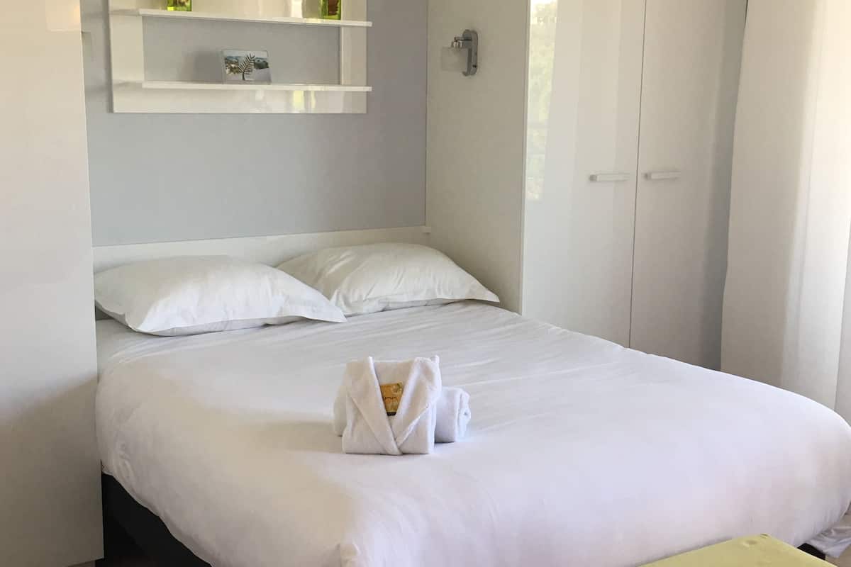 A neatly made bed with white linens, a bedside table, and a wardrobe in a hotel room.