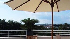 A wooden table and chairs under a large umbrella on an outdoor patio with a view of the city. - PAVILLON BEL AIR (Cannes)