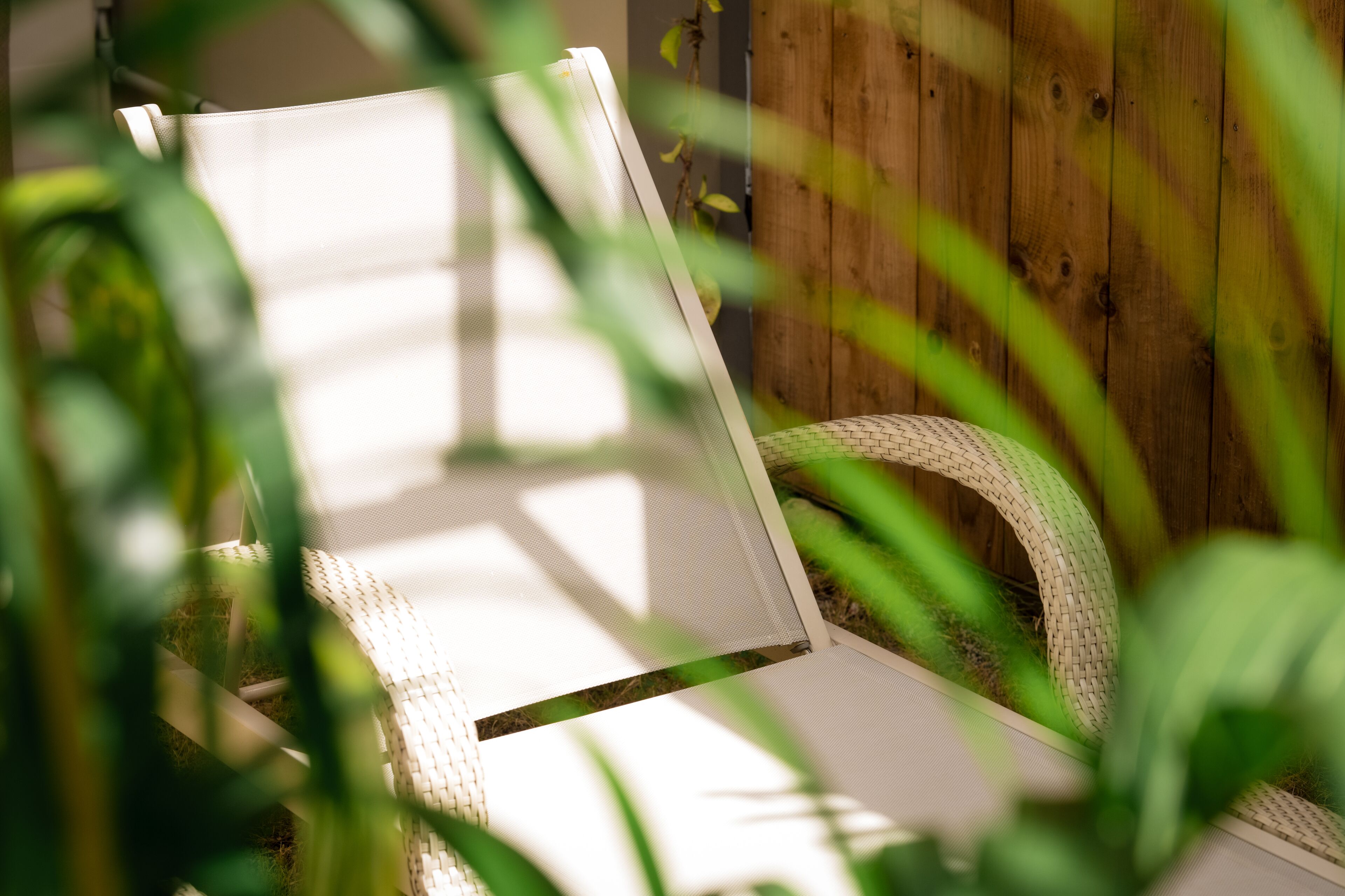 A wicker chair with a mesh backrest, positioned against a wooden wall.