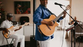 Una persona suona la chitarra in una stanza mentre, sullo sfondo, un'altra persona suona il basso.