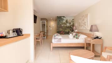 Une chambre d’hôtel avec un lit, une table de chevet, une lampe et une petite table en bois. Il y a également un coin cuisine avec une machine à café et des tasses.