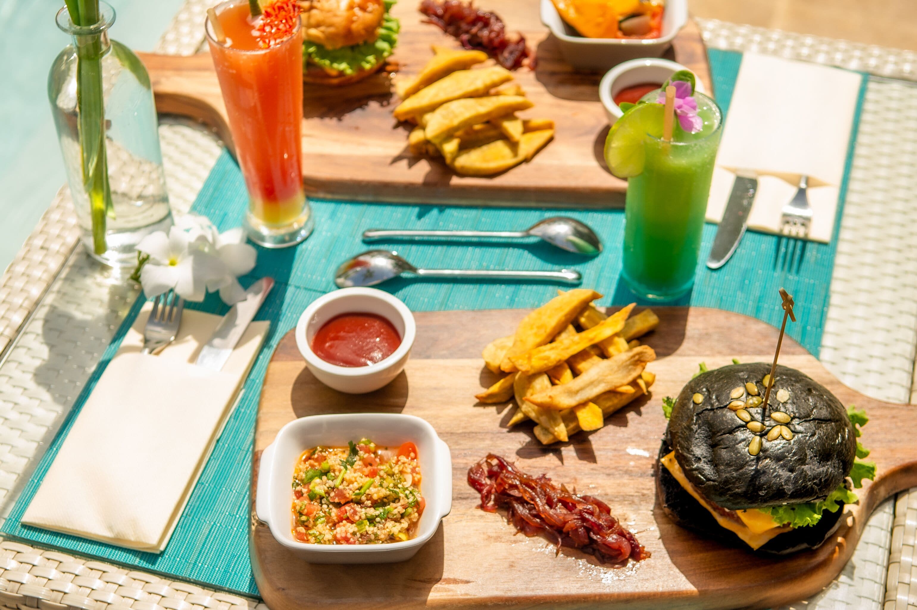 A meal with a burger, fries, and drinks on a wooden board.