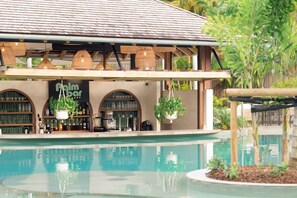 A poolside bar with a sign reading "Palm Bar," surrounded by a pool and potted plants.